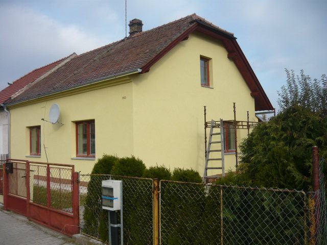 Rodinný dům se žlutou fasádou a lešením u štítu